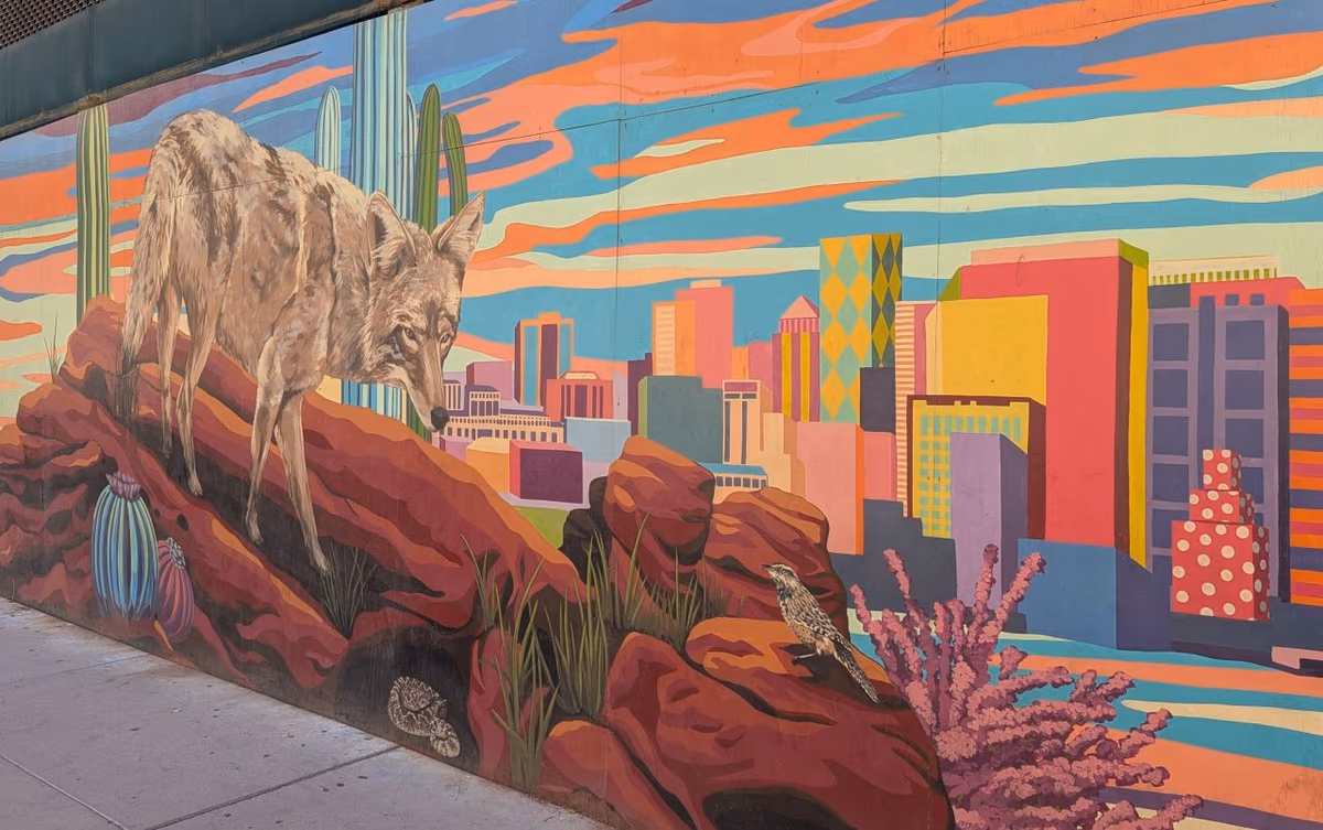 A vivid mural in Phoenix showing a coyote on red rocks above a stylized city skyline, with saguaro cacti and a cactus wren